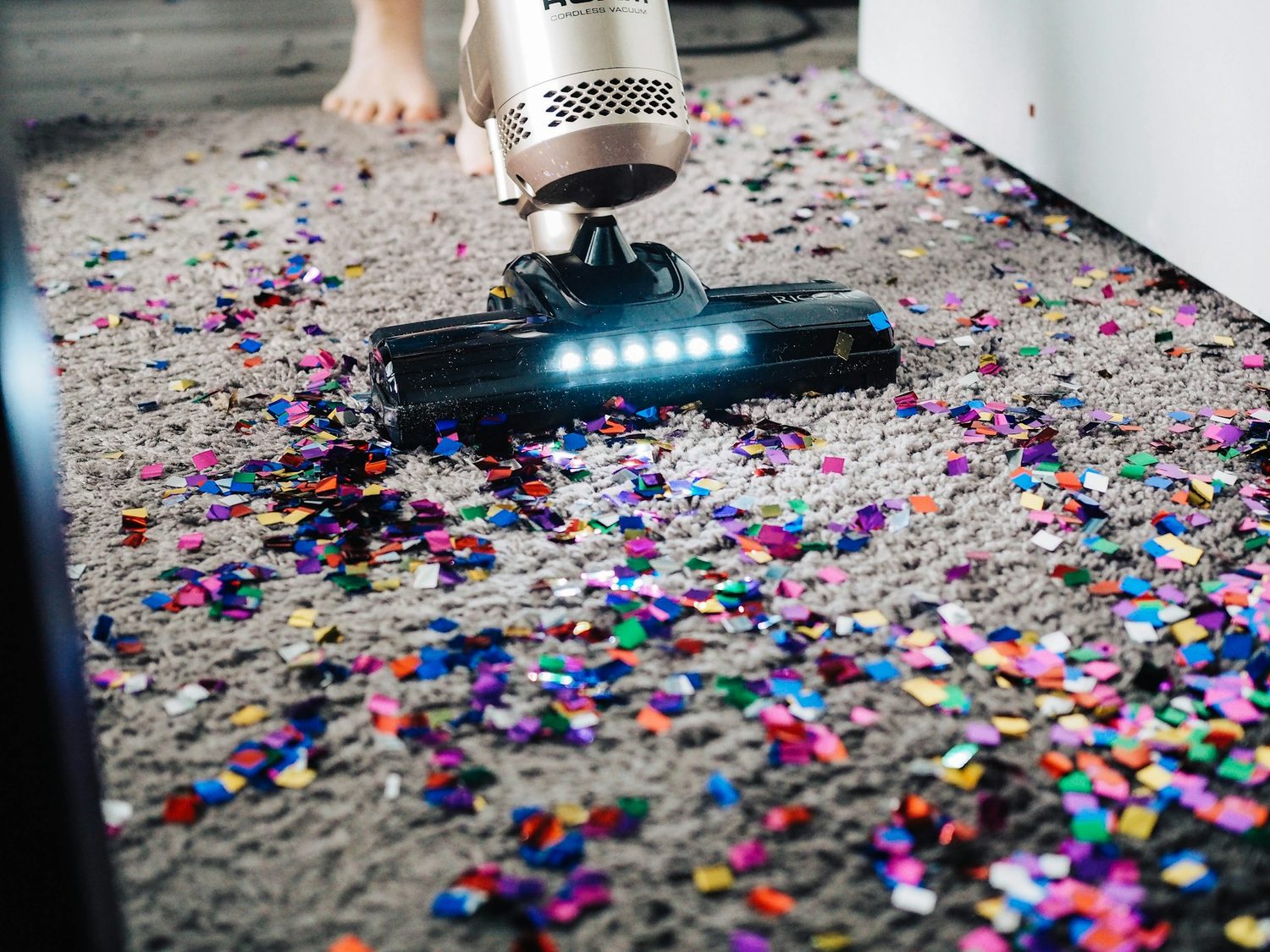 Aspiradora inalámbrica limpiando una alfombra cubierta de confeti de colores