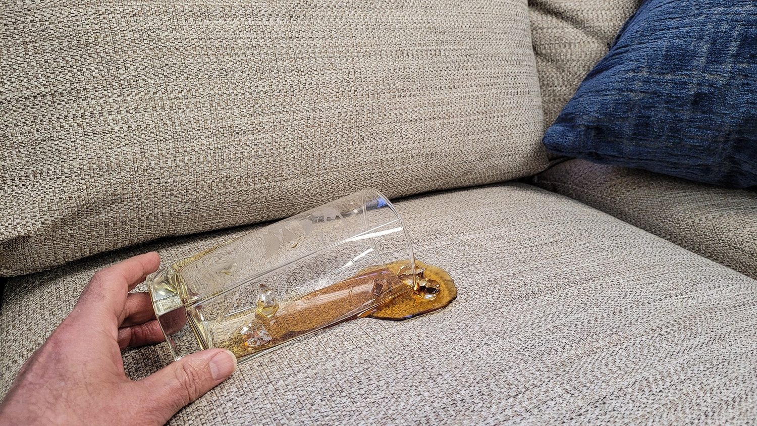 Una bebida se derrama de un vaso sobre el cojín de un sofá claro