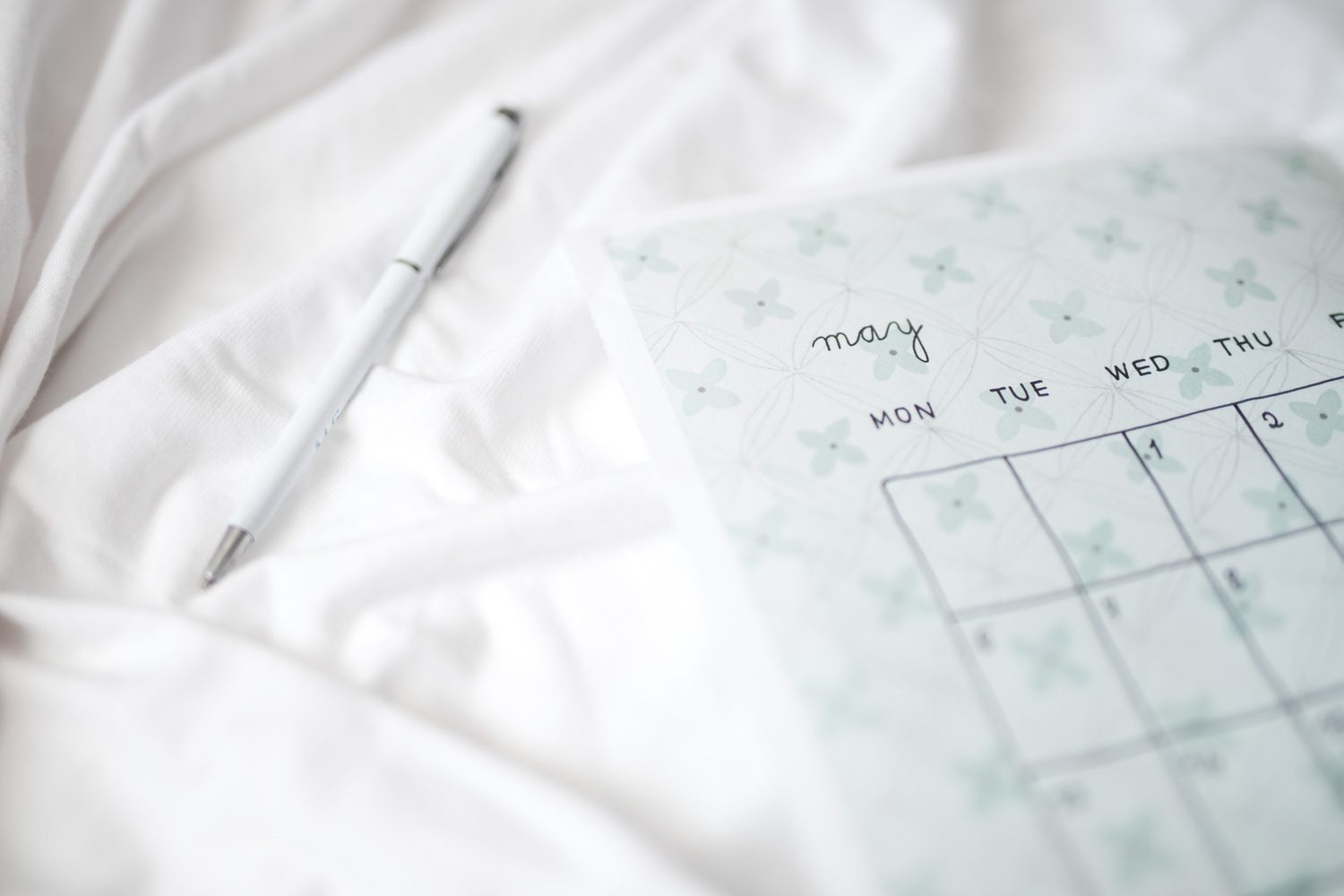 Calendario de mayo y bolígrafo blanco colocados sobre ropa de cama blanca