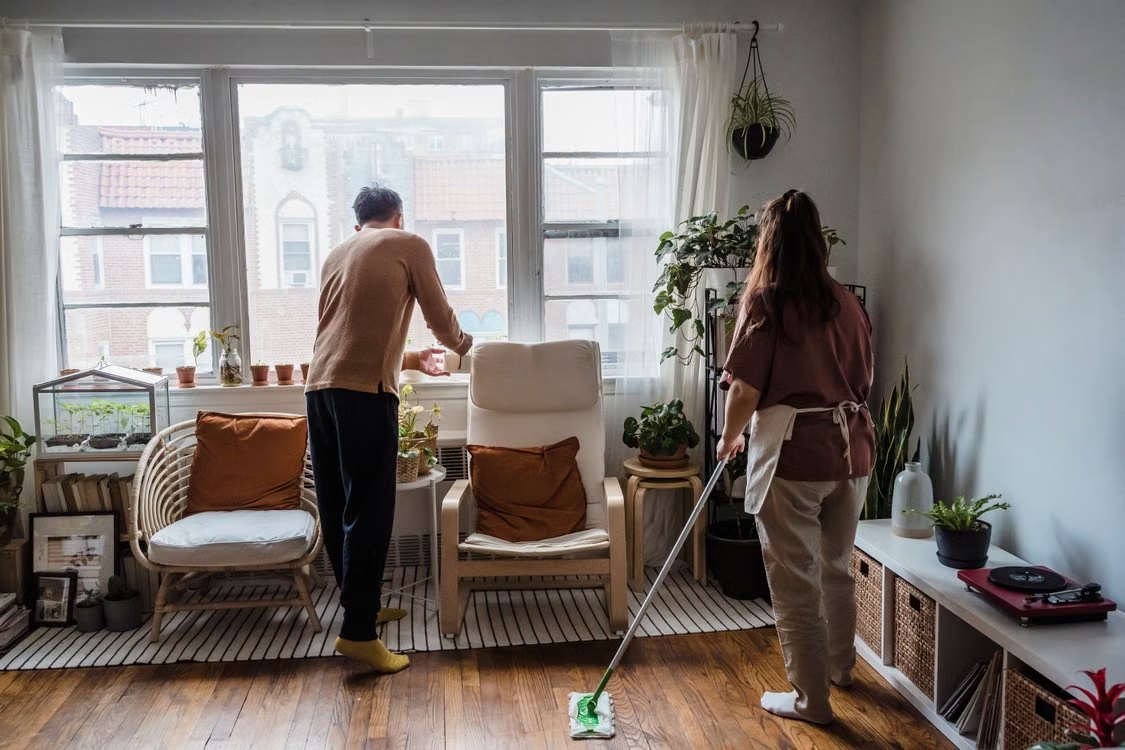 Dos personas ordenan un salón con plantas mientras una de ellas pasa la mopa