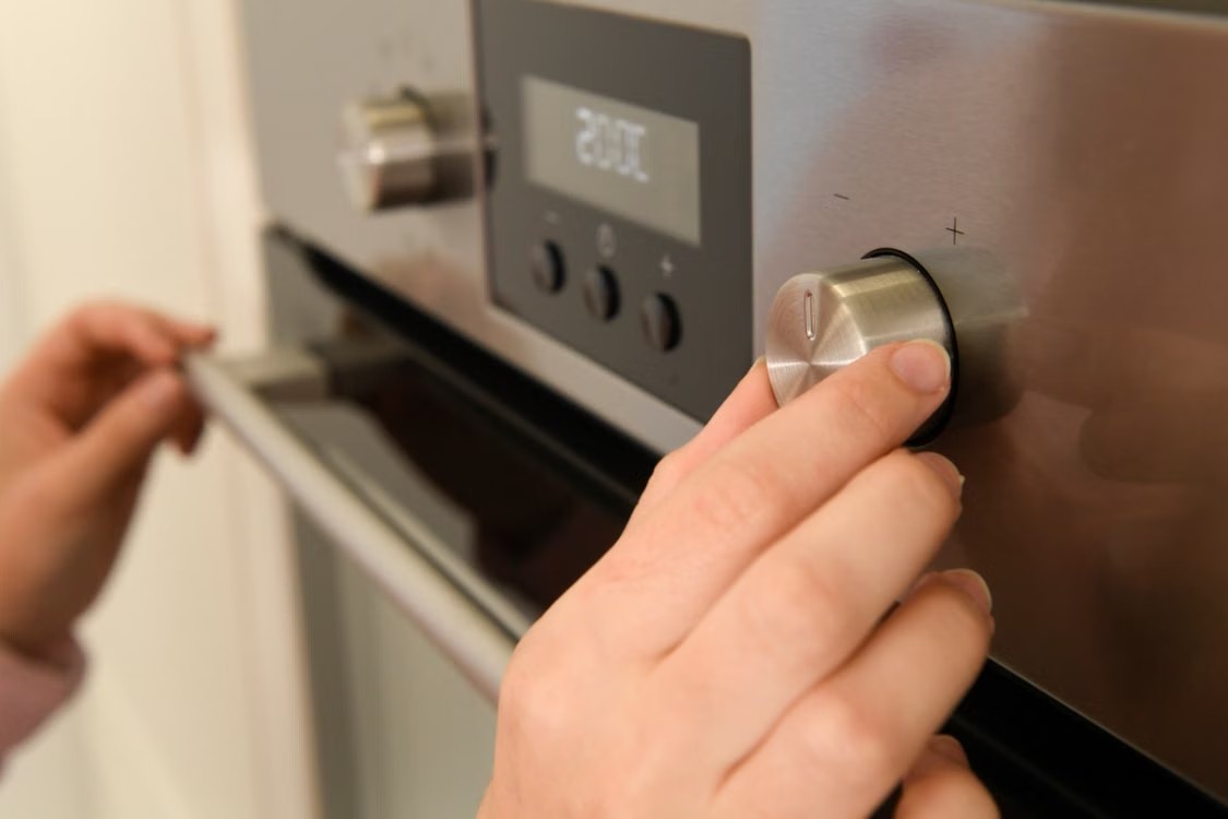 Mano ajustando el mando de temperatura de un horno de acero inoxidable