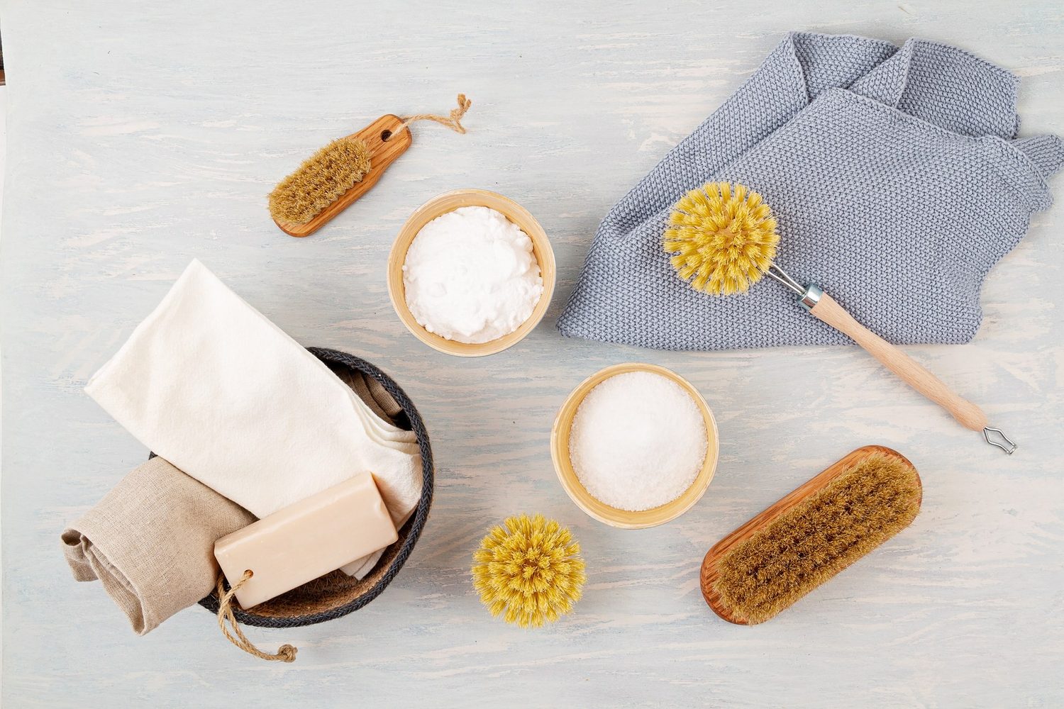 Paños, jabón, cepillos y recipientes con productos de limpieza sobre una mesa clara