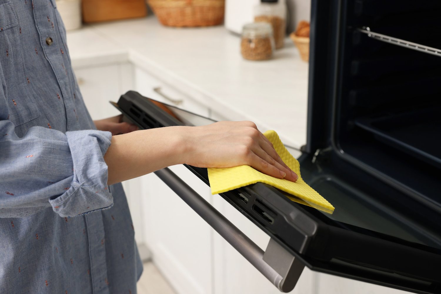 Persona limpiando la puerta abierta de un horno con un paño amarillo