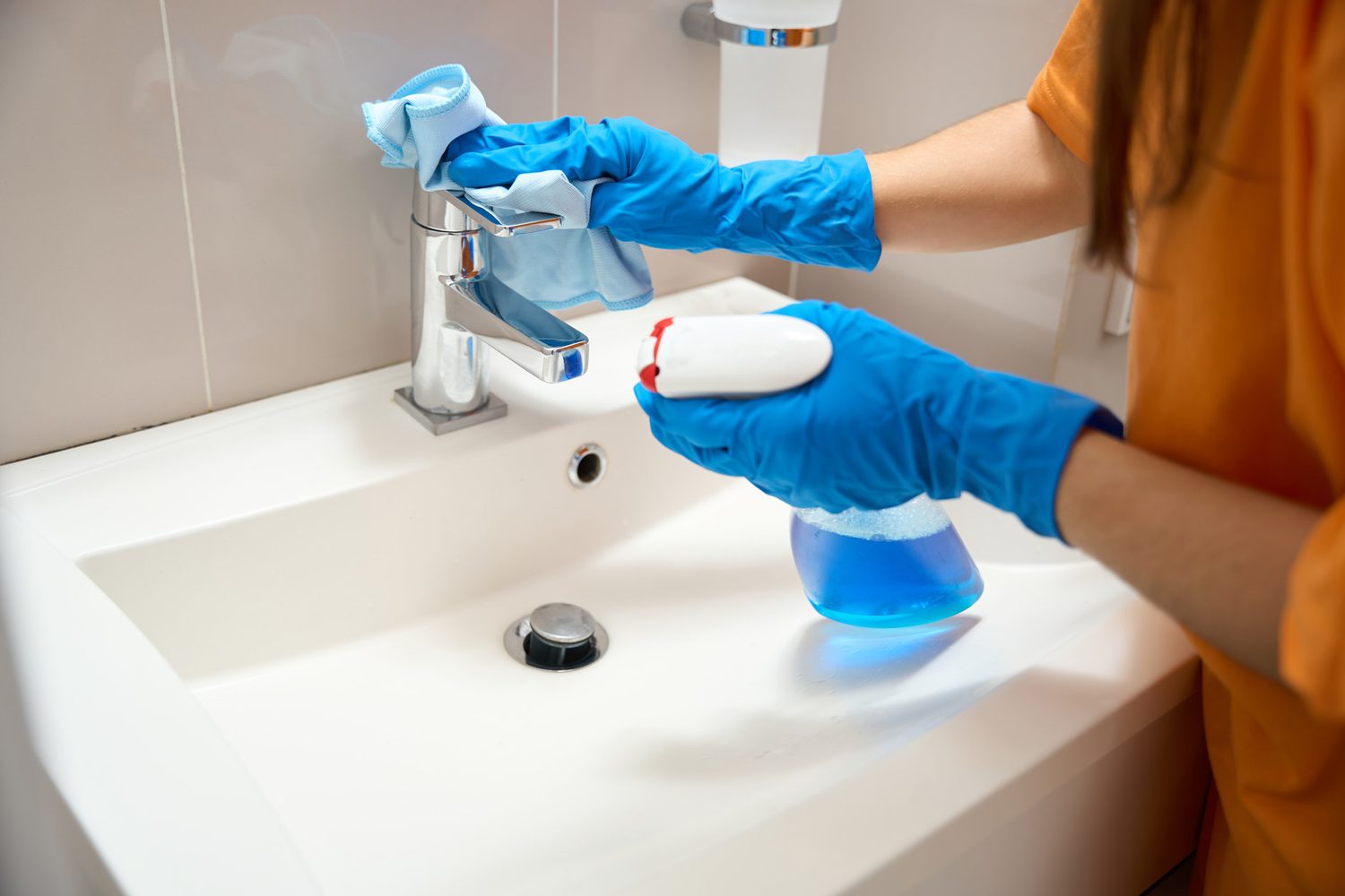 Persona con guantes azules limpia el grifo de un lavabo con un paño