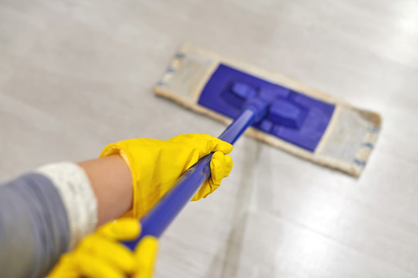 Unas manos con guantes amarillos manejan una mopa de cabezal plano sobre un suelo claro