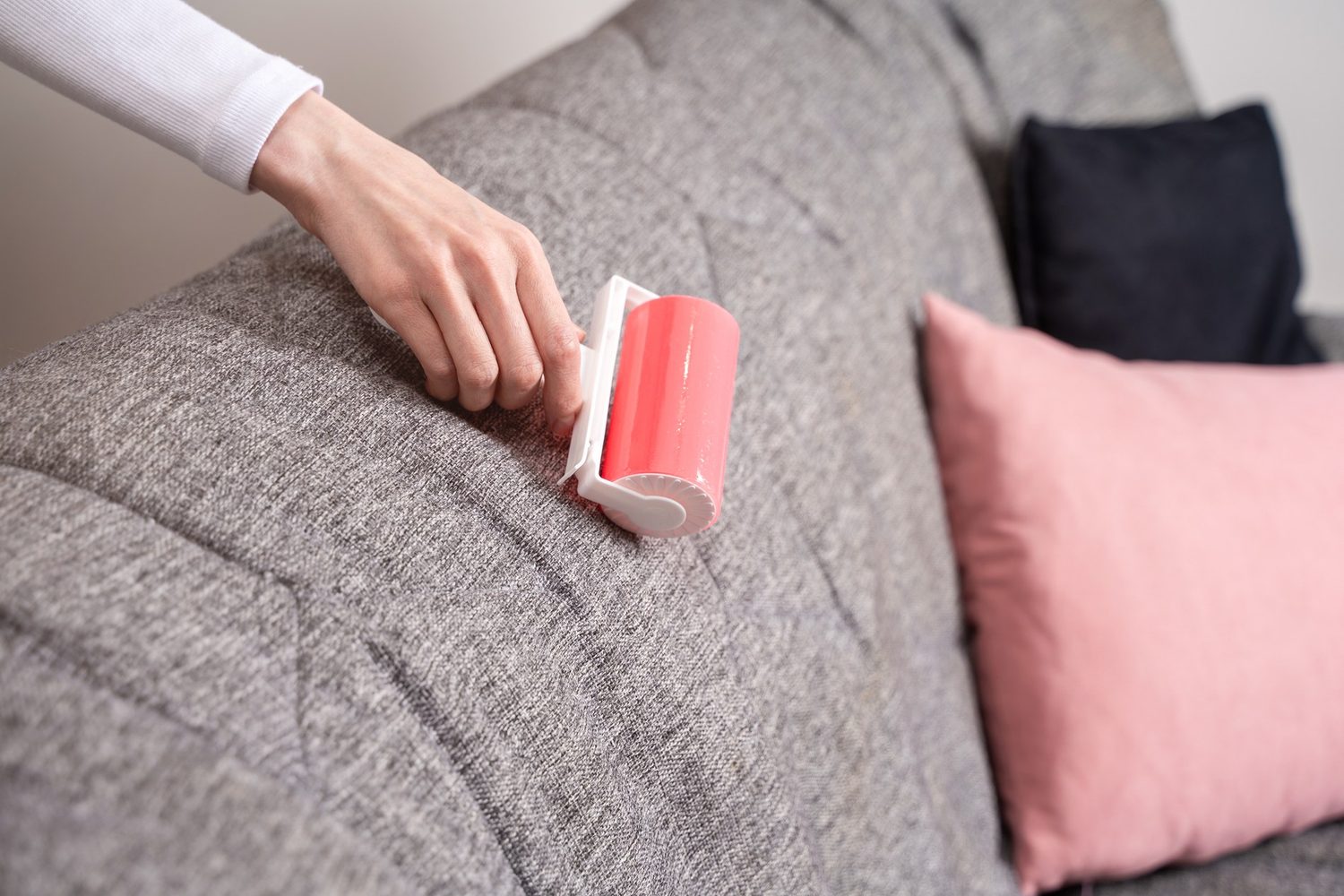 Mano pasa un rodillo adhesivo rojo por un sofá gris para retirar pelos y pelusas