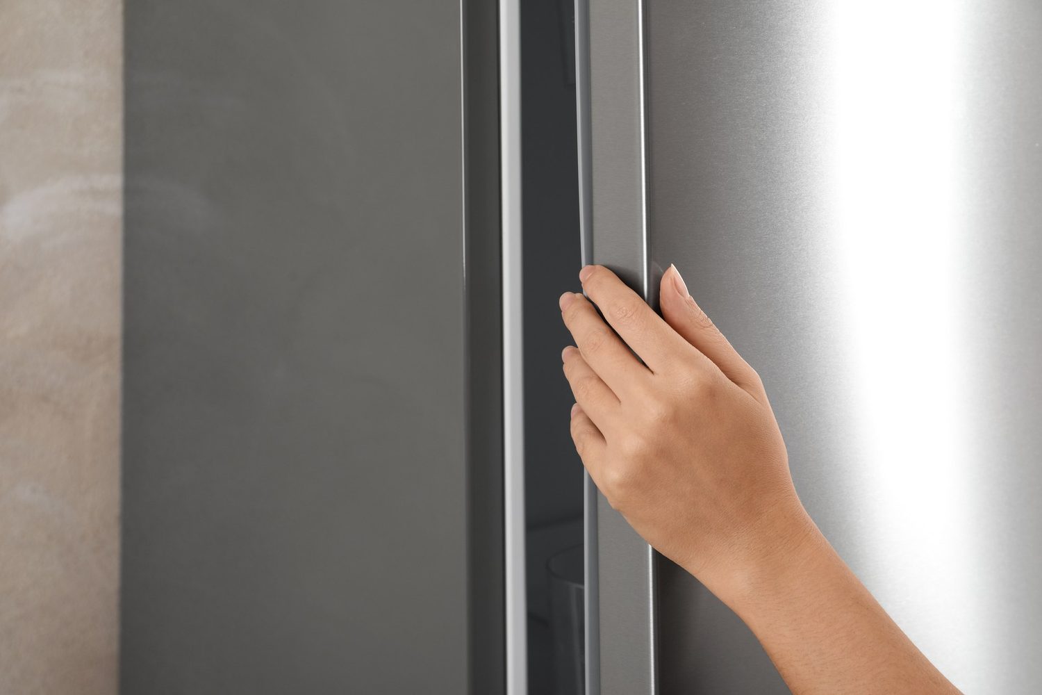 Una mano toca el tirador de la puerta de un frigorífico de acero inoxidable en la cocina