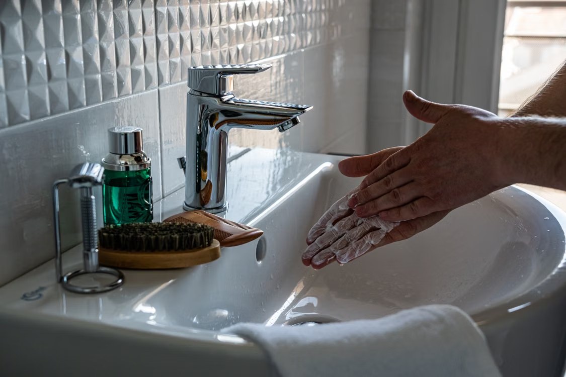 Unas manos enjabonadas se frotan sobre un lavabo junto a un grifo