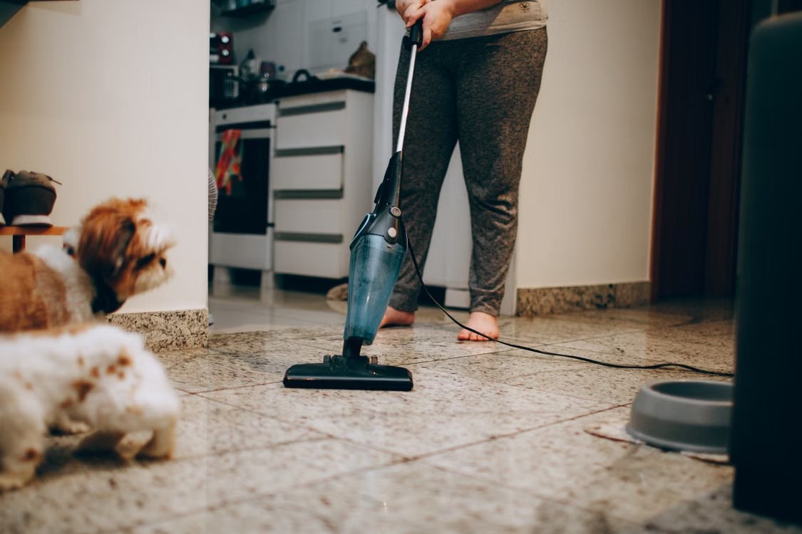 Una mujer aspira el suelo de casa mientras dos perros observan cerca
