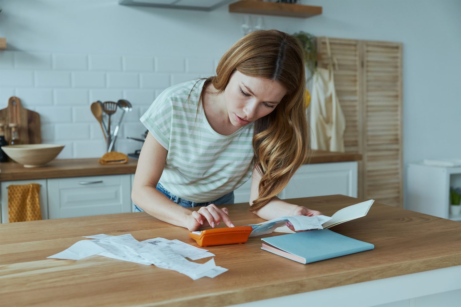 Mujer calcula su presupuesto doméstico con una calculadora y varios recibos sobre la mesa de la cocina