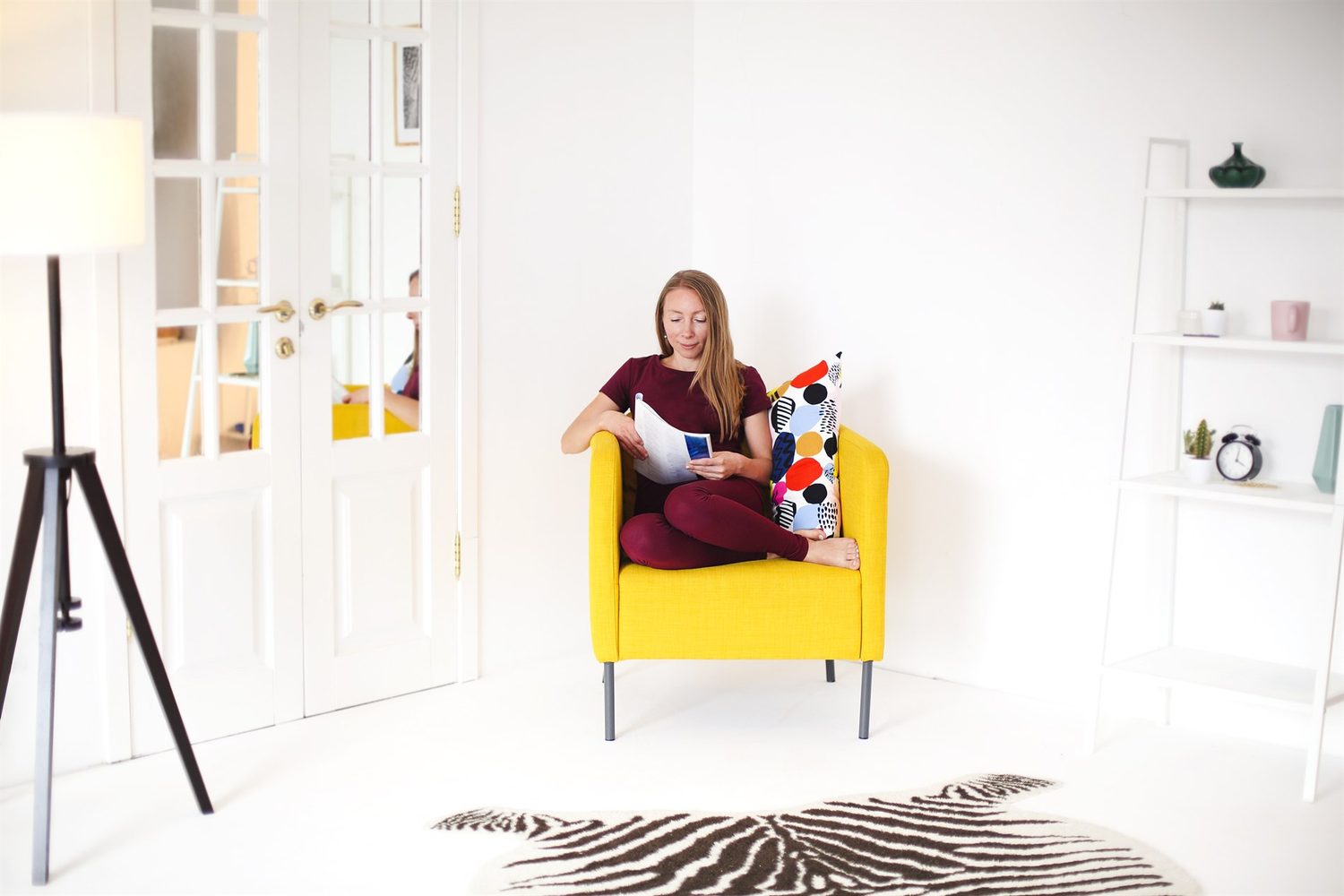 Mujer lee un libro en un sillón amarillo dentro de un salón luminoso y ordenado