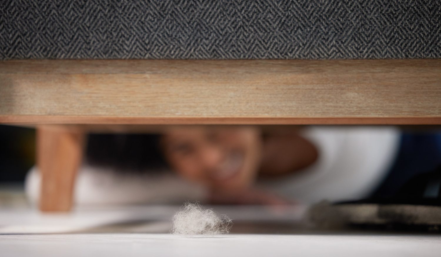 Acumulación de polvo bajo un sofá mientras una persona mira debajo