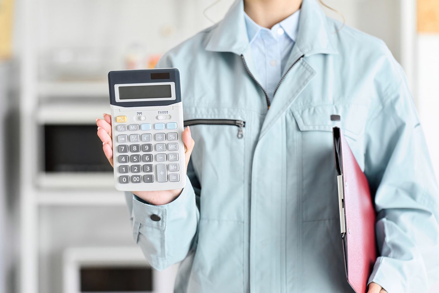 Primer plano de una persona con uniforme azul claro que muestra una calculadora y lleva un portapapeles rojo. Ilustra el cálculo de costes de un servicio de limpieza.