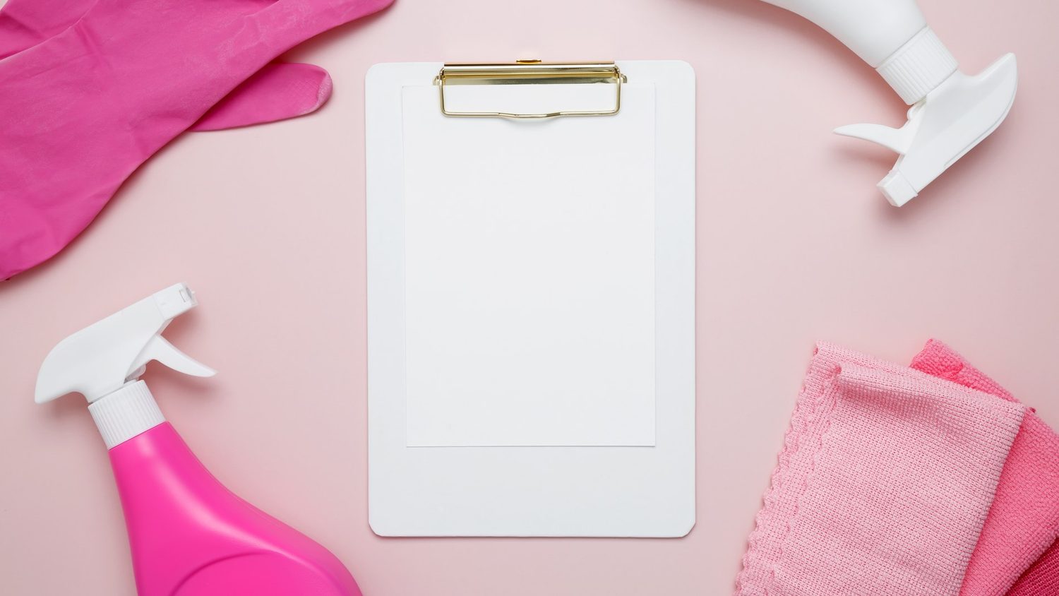Un portapapeles en blanco aparece rodeado de guantes, pulverizadores y paños de limpieza sobre fondo rosa