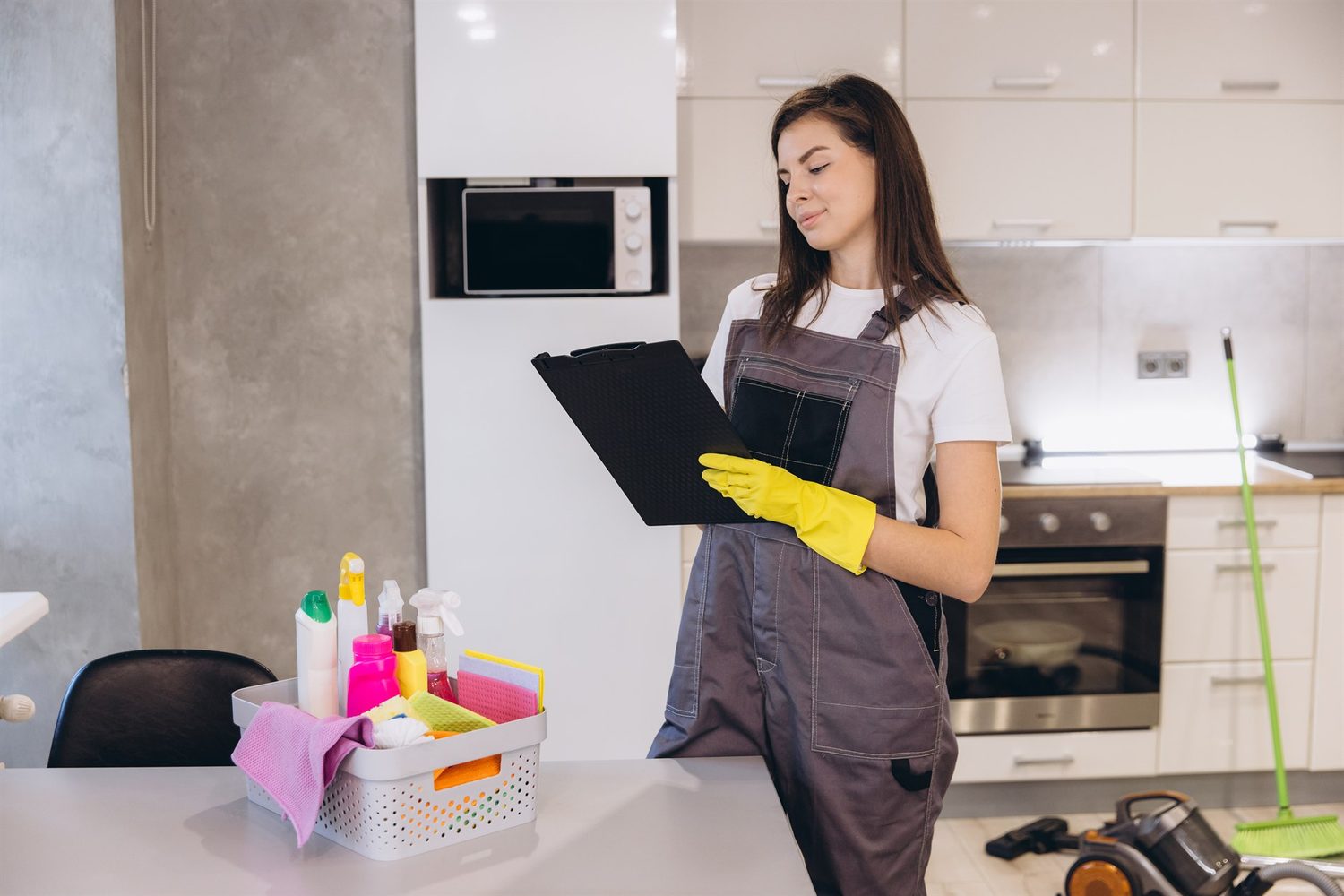 Una profesional de limpieza revisa un portapapeles junto a productos de limpieza en una cocina