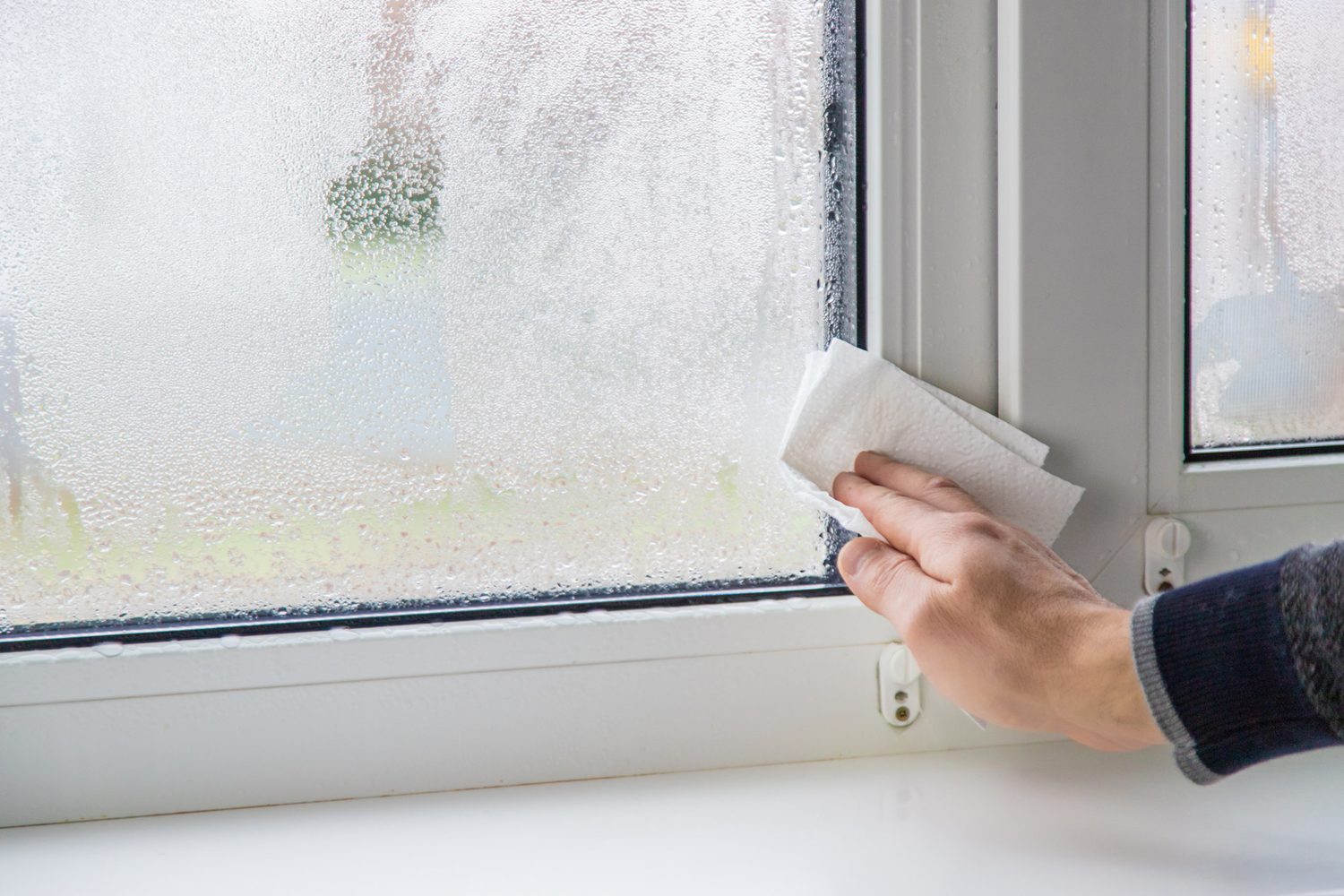 Una mano seca la condensación de una ventana con papel absorbente