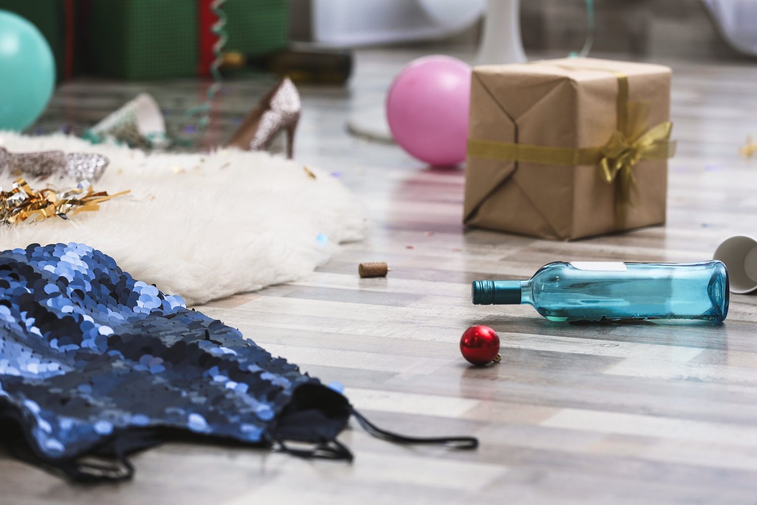 Suelo de salón desordenado tras una fiesta, con una botella, globos y objetos esparcidos